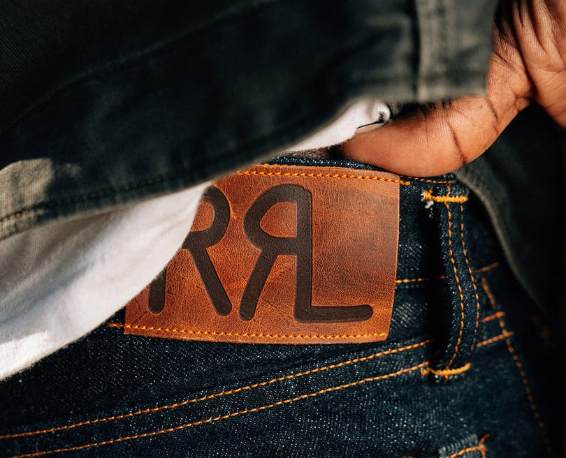 Close-up of a person wearing jeans with a visible brand logo.