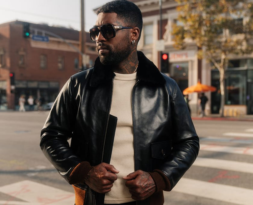 Man wearing a black leather jacket and sunglasses on a city street.