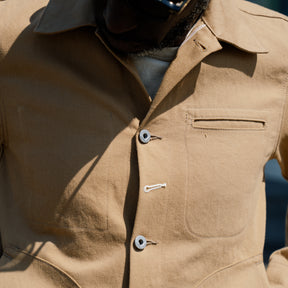 Close-up of a beige jacket with buttons and a pocket.
