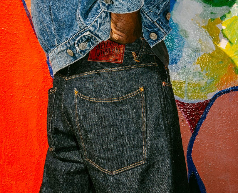 Person wearing a denim jacket and jeans with a colorful abstract painting in the background