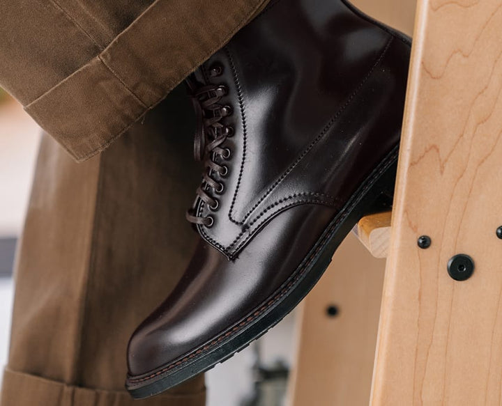 Black leather boot with brown trim on a wooden chair